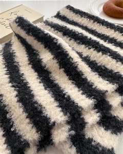 Close-up of black and white striped wool scarf with textured bouclé yarn on a table