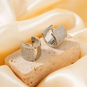 Detailed view of silver hoop earrings with pavé zircons on a beige stone and silk background