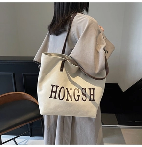 Detail of a large canvas tote bag with brown leather handles worn by a model in casual style