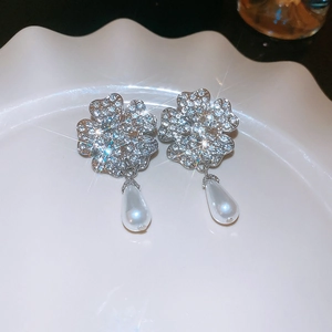 Detail shot of silver four-leaf clover earrings with crystals and drop pearls on a dish