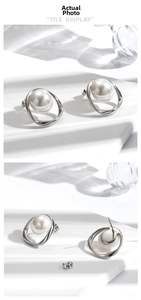 Detail view of pearl earrings with irregular silver metal rings on a stone surface
