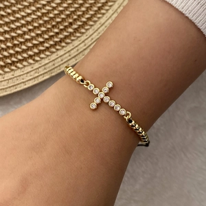 Macro detail of gold-plated beaded bracelet with micro-paved zircon cross charm pendant