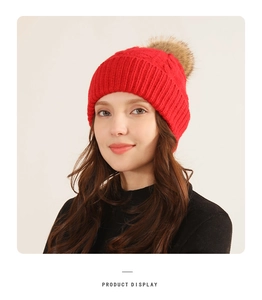 Detailed close-up of a red knitted winter hat featuring a faux fur pompom and cable texture