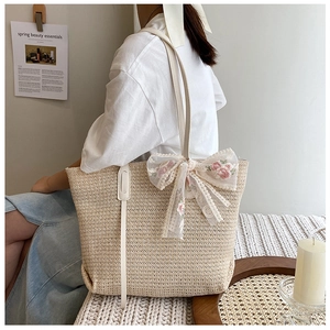Straw tote bag with lace bow accessory shown on shoulder in a minimalist setting