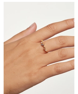 Detail of a thin gold band ring featuring multi-colored gemstones on a female hand