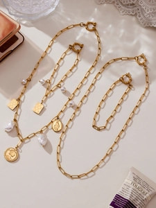 Detailed flat lay of golden paperclip chain necklaces with coin and pearl pendants