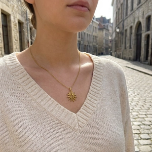 Golden sun pendant necklace with spiral center on a model wearing beige knit sweater