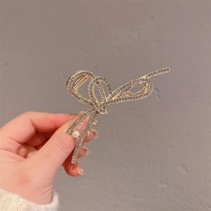 Détail d'une pince à cheveux dorée en forme de nœud avec strass brillants et perle