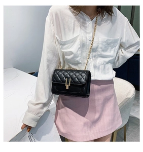 Detail of black quilted chain bag with gold H-shaped lock worn by model in white shirt