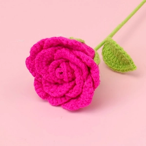 Macro shot of a handmade crocheted pink rose with green leaves on a soft pink background