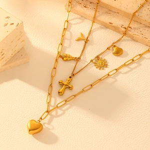 Gold double-layer necklace with heart, cross, and seashell charms on a stone display