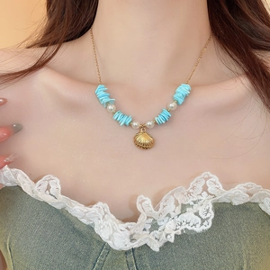 Close-up of ocean-themed necklace with gold seashell, blue stones, and white pearls
