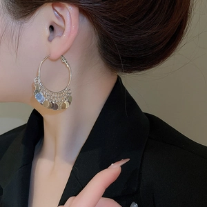 Close-up side view of a model wearing large silver sequin tassel hoop earrings