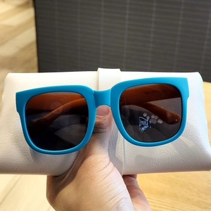 Détail de lunettes de soleil pliables bleues pour enfants avec étui en cuir blanc