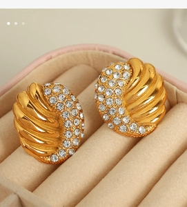 Macro view of gold-tone wing earrings with pavé crystals in a beige velvet gift box