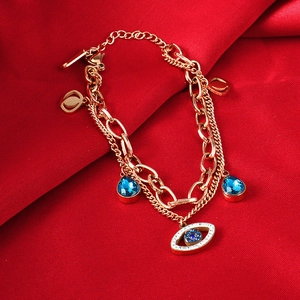Detail of rose gold evil eye bracelet with blue teardrop gems on red silk fabric