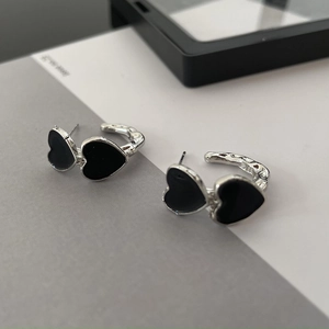 Macro detail of silver C-shaped hoop earrings with two polished black enamel hearts