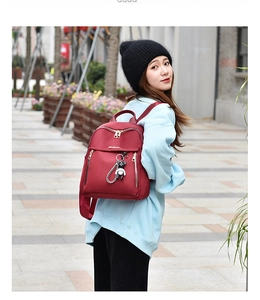 Detail of burgundy oxford backpack with gold zippers and cute bear charm on a female model