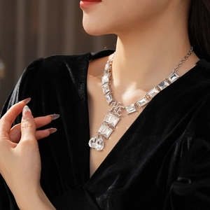 Close-up of silver necklace featuring square crystals and heart pendant with logo detail