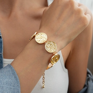 Detailed close-up of a gold coin link bracelet with vintage relief patterns on woman wrist