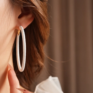 Close-up of a model wearing large white textured leather hoop earrings with gold pins