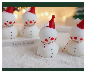 Détail d'une bougie bonhomme de neige avec chapeau rouge et écharpe rayée sur socle enneigé