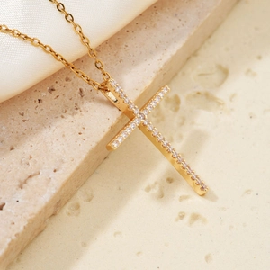 Elegant gold cross necklace with white zircon crystals on a luxury stone and silk background