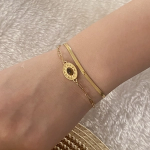 Detail of layered gold bracelet featuring a flat snake chain and brown gemstone pendant