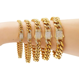 Five gold stainless steel Cuban link bracelets with iced-out buckles on a male wrist