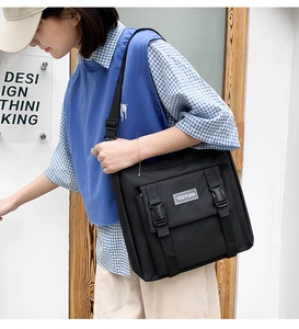 Detail of black canvas messenger bag featuring plastic buckles and adjustable strap on a model