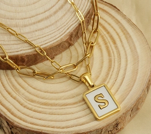 Detail of 18K gold paperclip necklace with rectangular letter S pendant on wood