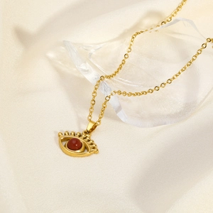 Golden necklace with red devil eye pendant displayed on elegant silk and crystal