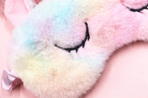 Macro detail of rainbow gradient plush fabric with delicate eyelash embroidery on eye mask