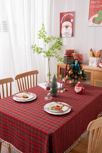 Close-up of red Christmas plaid tablecloth with tassel edges and festive dinnerware