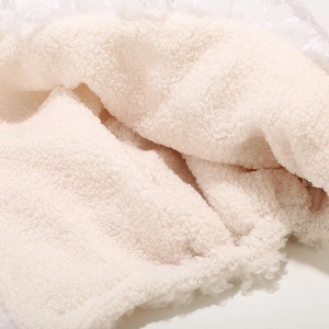Detail of plush lamb wool texture and delicate white lace trim on a cozy winter hat