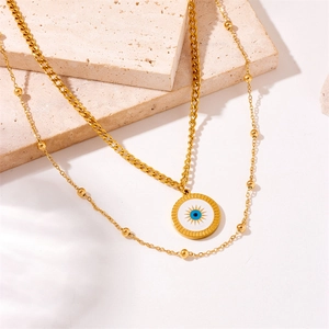 Detail of layered gold necklace featuring evil eye disc pendant and bead chain textures