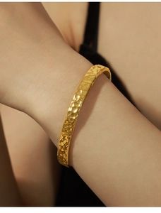 Dettaglio della superficie martellata dorata di un bracciale a fascia in acciaio