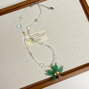 Dettaglio di una collana di perline boho con un ciondolo a forma di palma verde e marrone