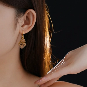 Close-up of geometric diamond-shaped gold earrings with amber crystals on model