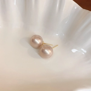 Detailed macro view of champagne pearl stud earrings with gold finish on a shell tray