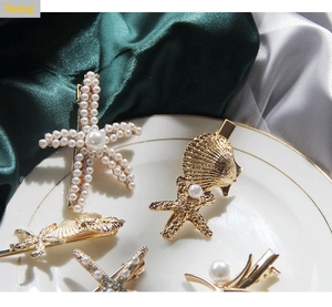 Detail of gold starfish and shell hair clips with pearls on a luxury satin background