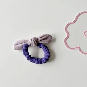 Detail view of a dual-tone purple suede bow hair tie with soft textured fabric