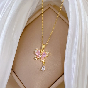 Dettaglio macro della collana a farfalla dorata con zirconi rosa su seta bianca