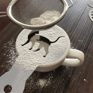 Detailed view of cat-shaped coffee stencil being used with a powder shaker over a cup