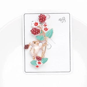 Macro detail of enamel squirrel brooch with berries and flowers on card