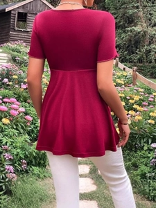 Short sleeve burgundy maternity dress with V-neck and ruffled hem shown in a garden setting