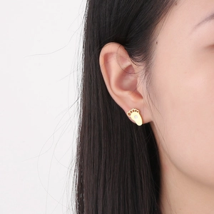Close-up of a golden paw print stud earring with a small crystal on a female ear