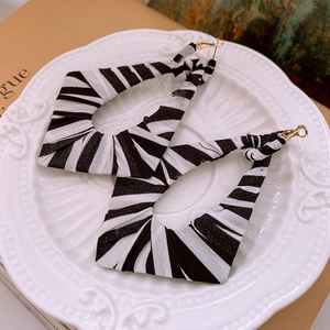 Detailed view of geometric silver earrings with zebra pattern fabric wrap on a white plate