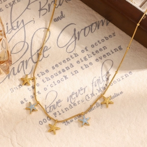Macro view of 18K gold plated necklace featuring colorful starfish charms on a vintage script