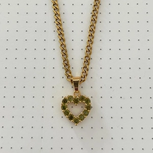 Detail of a golden heart pendant set with yellow-green zircons on a curb chain
